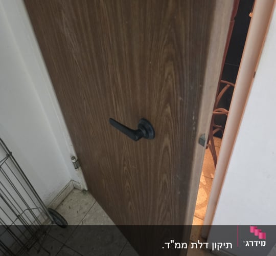 דלת עץ עם ידית שחורה פתוחה מעט